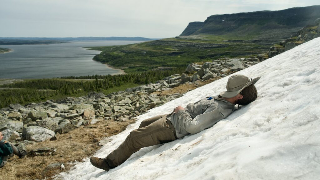 Person relaxing on snowy mountain terrain overlooking lake.