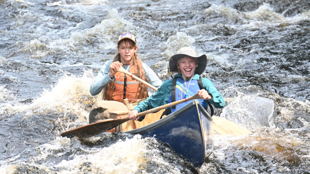 Two people canoeing in rapid river waters.